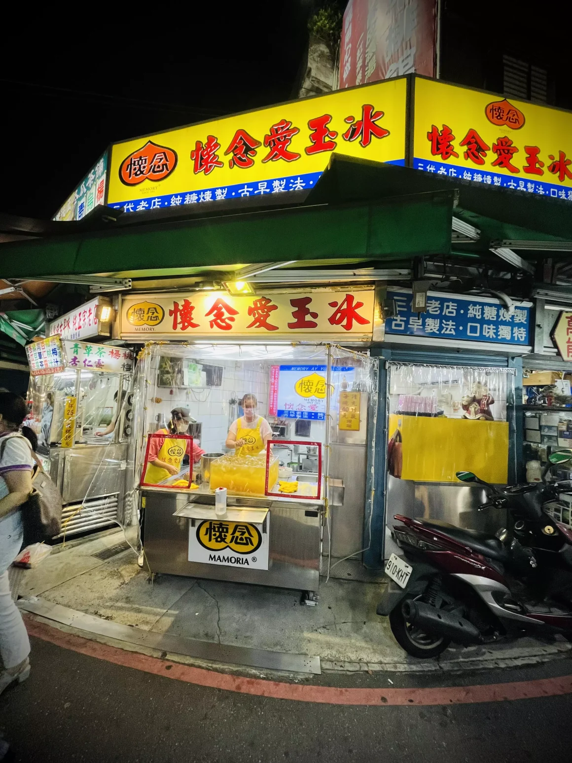 【萬華夜市】《懷念愛玉冰》:一半是回憶的召喚術,另一半是長大後的誠實豆沙包 19 萬華懷念愛玉冰的攤位夜間全景,燈火通明的攤位前有顧客等候,店員正在不鏽鋼餐車內製作愛玉冰。