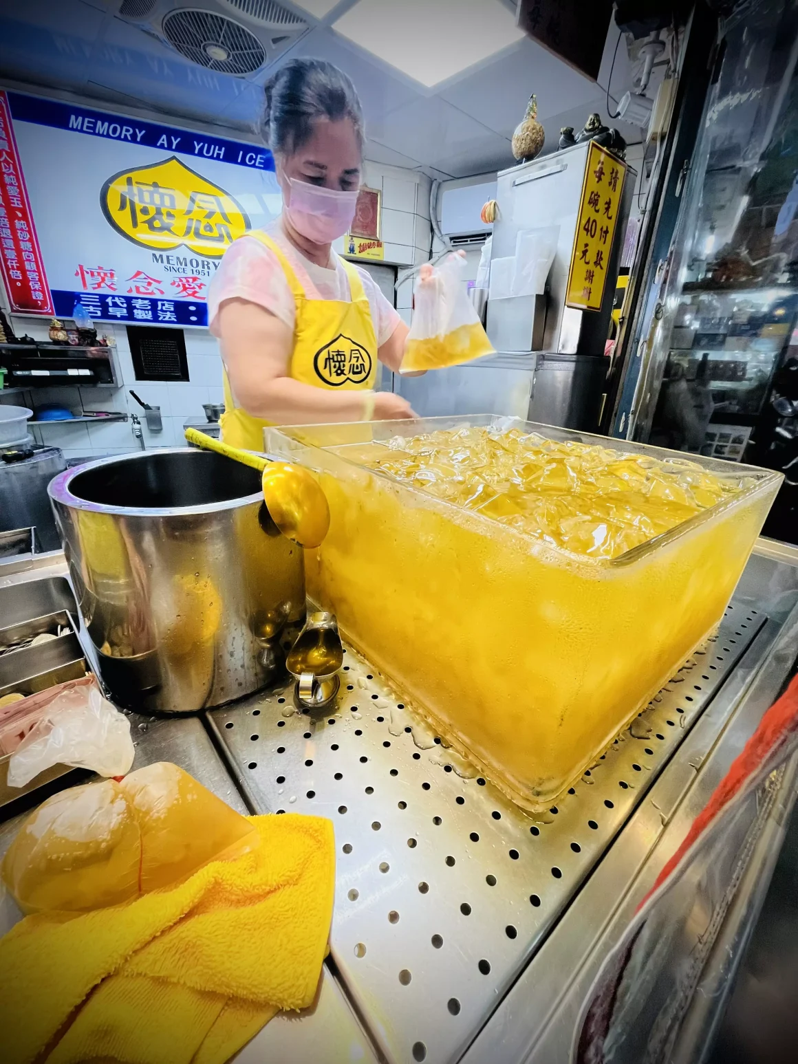 【萬華夜市】《懷念愛玉冰》:一半是回憶的召喚術,另一半是長大後的誠實豆沙包 14 萬華懷念愛玉冰的店員,正從一大盆冰涼的愛玉中,將黃澄澄的愛玉與糖水舀進傳統的塑膠袋裡,準備給客人。
