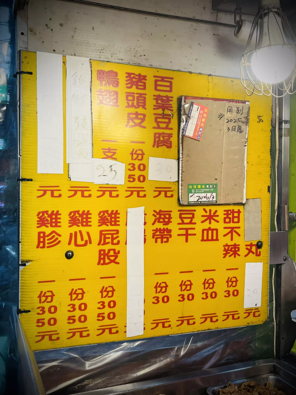 【板橋】《尚佳滷味》評價:一半是錢包的摯友,另一半是追劇的稱職配角 10 板橋尚佳滷味攤的黃色價目表,上面用大字寫著百葉豆腐、雞胗、米血等品項與價格,部分價格有塗改痕跡,充滿歲月感。