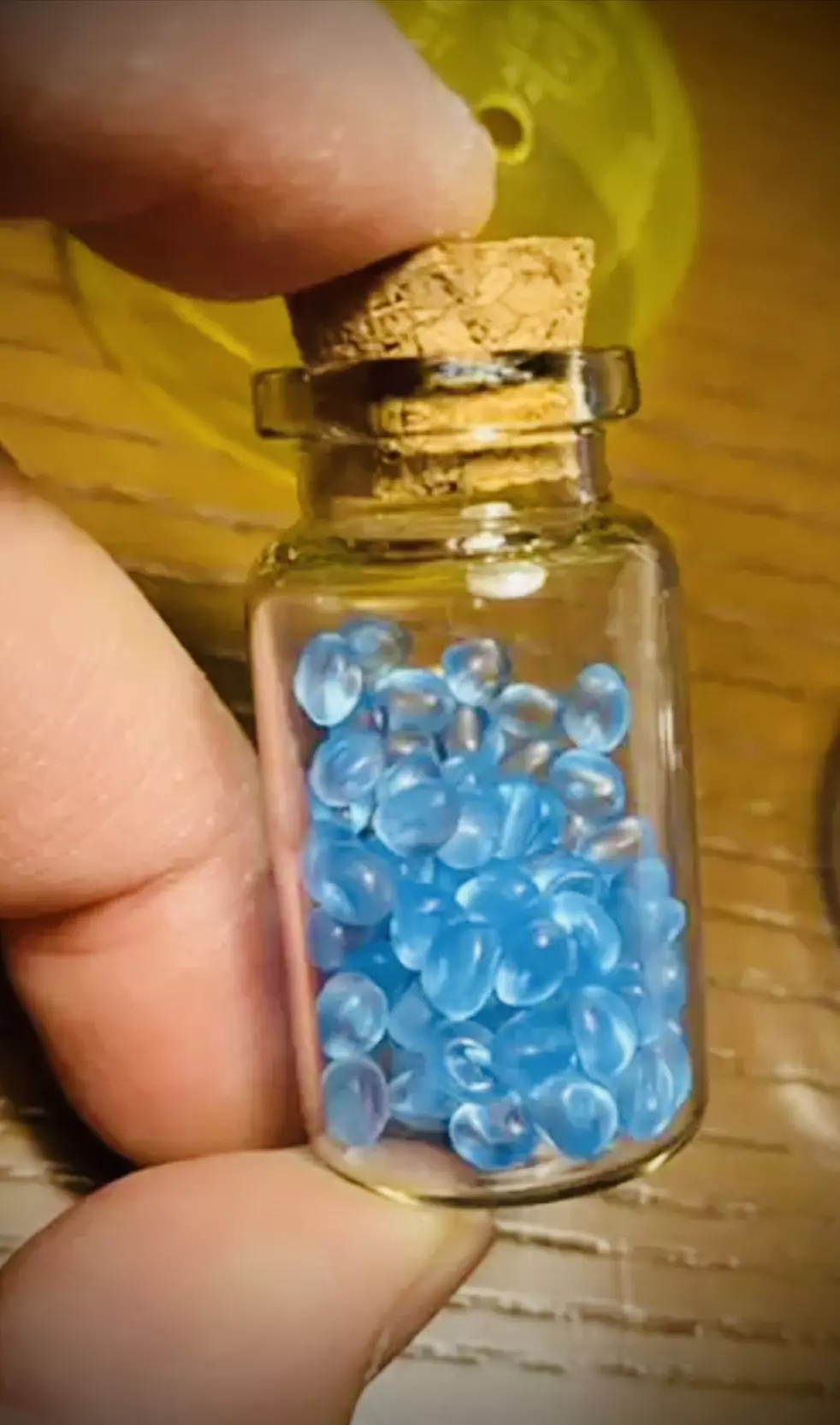 《香香豆》:一半是文具店的魔法藥水,另一半是口袋裡的香氣結界 14 一隻手拿著裝有藍色香香豆的玻璃小瓶,瓶口用軟木塞塞住,是台灣文具店販售的懷舊童年小物。