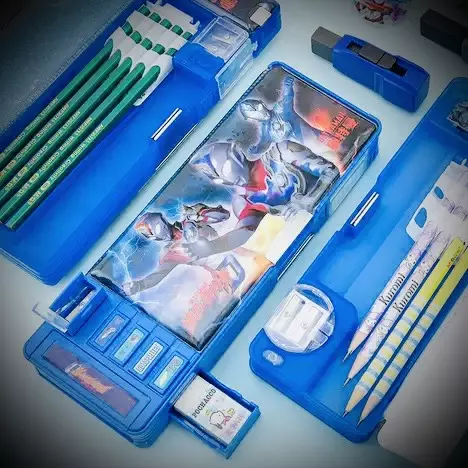 《機器人鉛筆盒》:一半是柑仔店的變形金剛,另一半是怕撞衫的童年虛榮 10 一個藍色的多功能機器人鉛筆盒,上面印有鹹蛋超人的圖案,鉛筆盒已打開並裝有各式文具,展示其多樣功能。