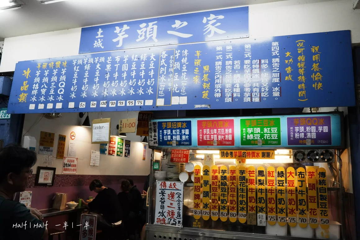 【土城】《芋頭之家》評價:一半是熱鬧的配料派對,另一半是C位出道的神級芋頭 8 「土城芋頭之家」冰店的店面,藍色的長條招牌上列出芋頭牛奶冰等各式冰品與價格,櫃檯前擠滿了點餐的顧客,呈現熱鬧的景象。